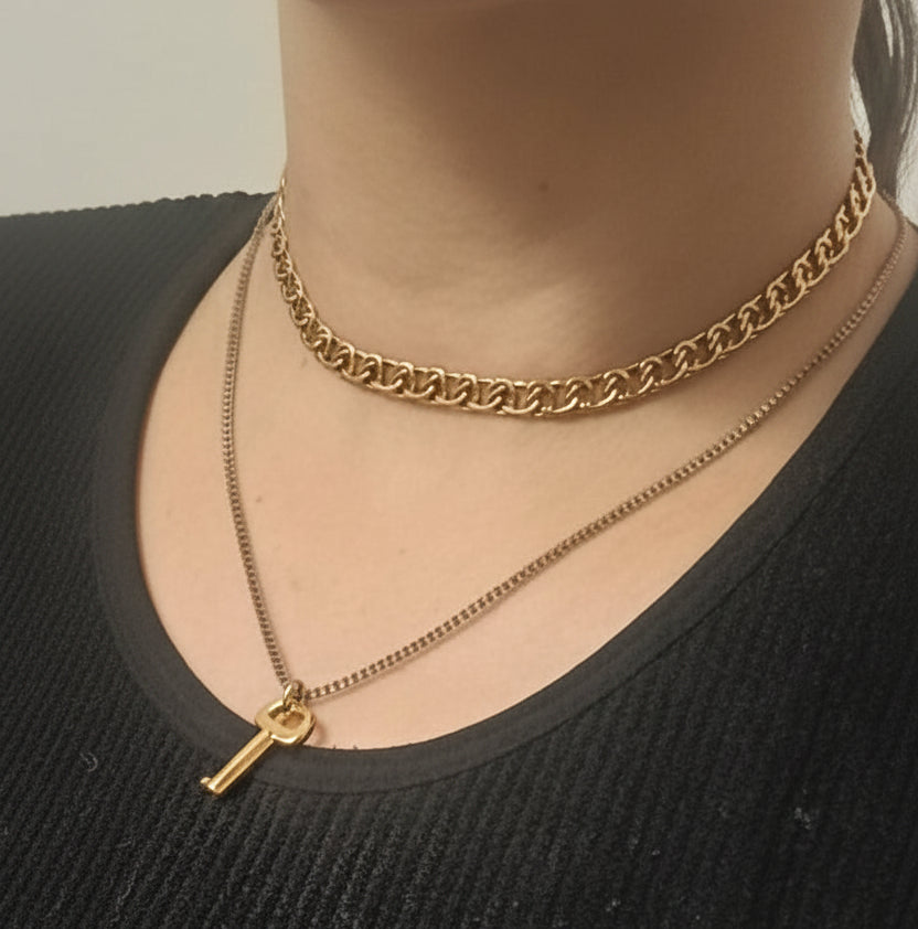 vue rapproché d'un cou de femme portant des bijoux. le collier ras le cou est doré, et le collier avec pendentif (la chaine est argenté, et le pendentif en forme de clé est doré)